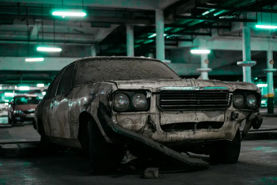 A dust-covered, rusted old sedan sitting in a dim parking garage