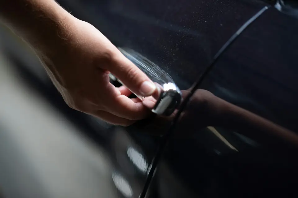 A hand reaching for the door handle of a dark car