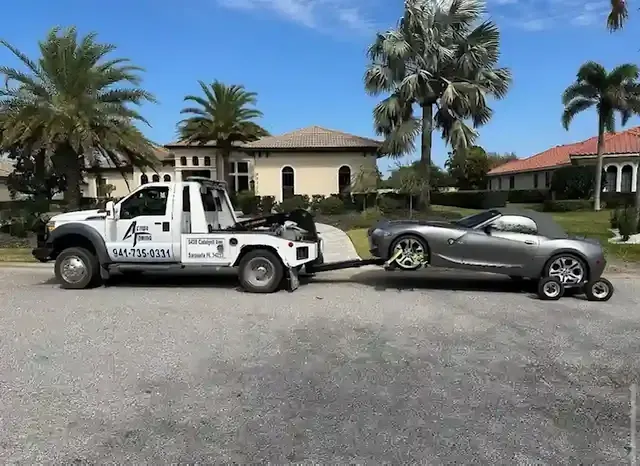 White Action Towing wrecker towing a silver convertible past palm trees on a Sarasota residential street